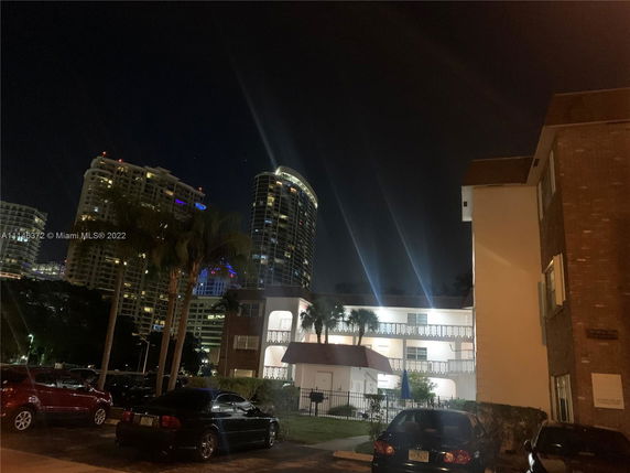 Night view of a residential building with illuminated high-rise buildings in the background.