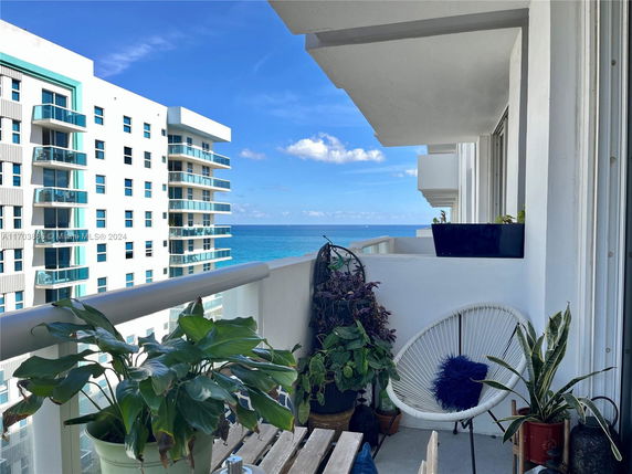 View of surrounding high-rise buildings and ocean from a balcony with potted plants and a chair.