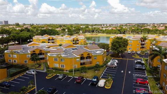 Aerial view of a residential complex with yellow buildings, a central parking area, and a nearby lake.