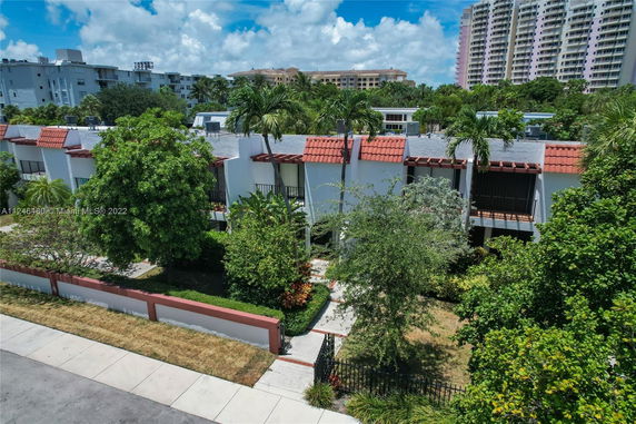 View of a series of white residential buildings with red roofs surrounded by trees and greenery.