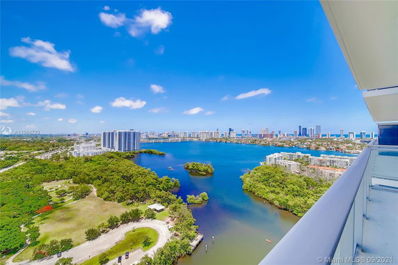 Panoramic view from a high-rise building showing a cityscape with tall buildings, a large body of water, and surrounding greenery.