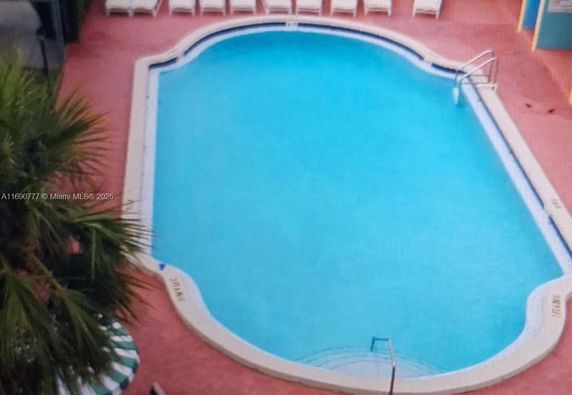 Overhead view of a swimming pool surrounded by a paved area with lounge chairs.
