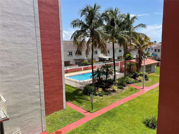View of a swimming pool area surrounded by residential buildings and palm trees.