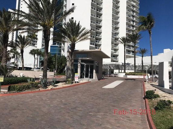 Front view of a high-rise building with palm trees along the entrance pathway.