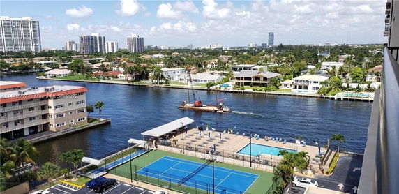 View from a building showcasing a river, nearby residential houses, and a sports complex with tennis courts.