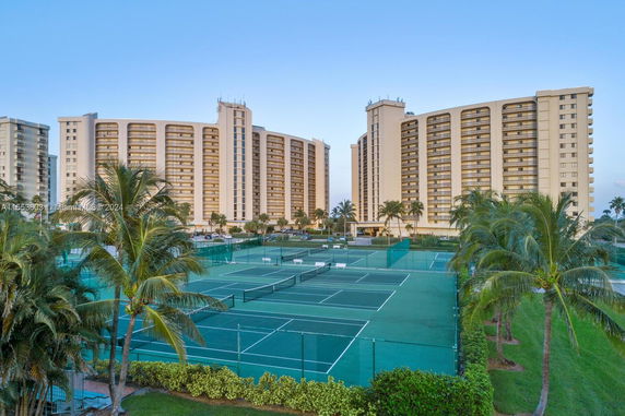 View of large residential buildings with a tennis court in the foreground.