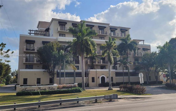 Front view of a multi-story residential building with balconies and palm trees.