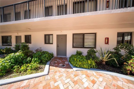 Exterior view of a building corridor with multiple doors and windows, surrounded by plants.