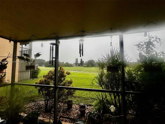 View from a covered patio with plants looking out to a grassy field.