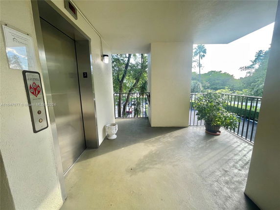 Exterior view from a building corridor with an elevator and outdoor railing.