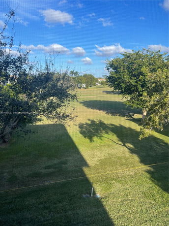 View from a building showing a grassy area with trees and a clear blue sky.
