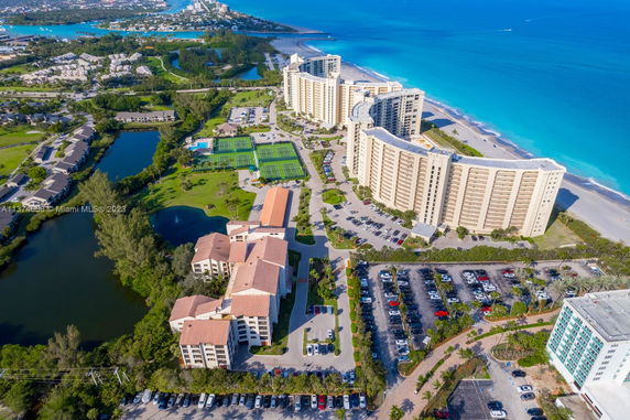 Aerial view of residential buildings and coastline with tennis courts and parking areas.