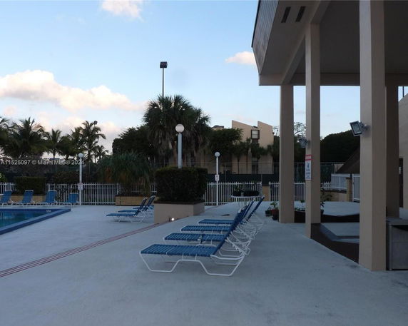 Outdoor swimming pool area with lounge chairs and surrounding palm trees.