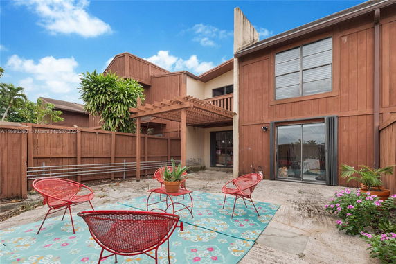 Outdoor view of a wooden townhouse with a patio area, featuring red chairs and a patio covering.