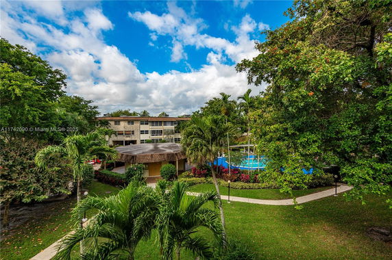 View of an outdoor area with a residential building in the background, surrounded by lush greenery and gardens.