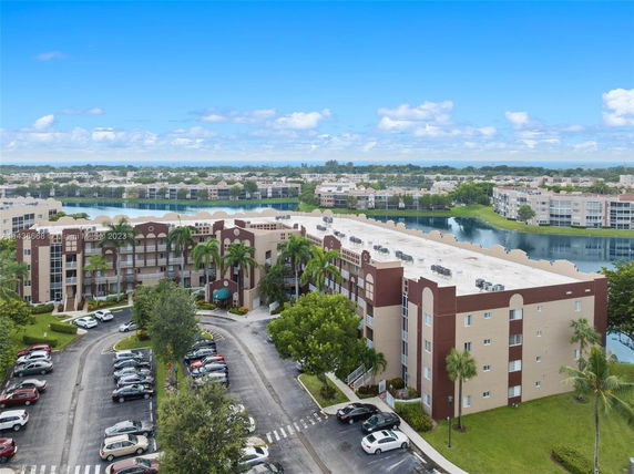 View of a large multi-story residential building complex with parking area and landscape, surrounded by other buildings and a water body.