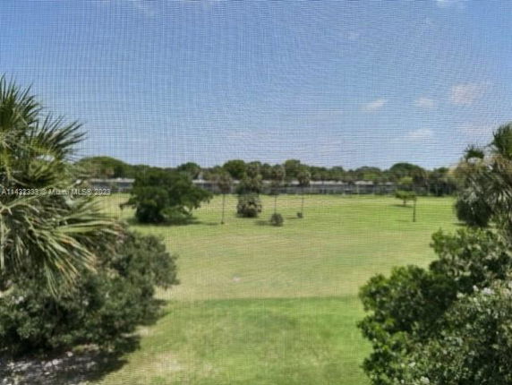 View of a grassy area with trees and a distant waterbody under a clear sky.