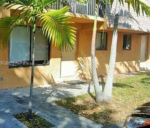 Front view of a building with small windows and an entrance, surrounded by palm trees.