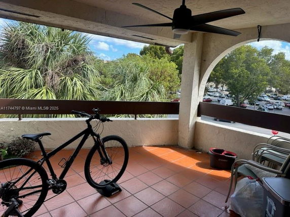 Outdoor view from a terrace with a bicycle and garden chairs, overlooking trees and parked cars.