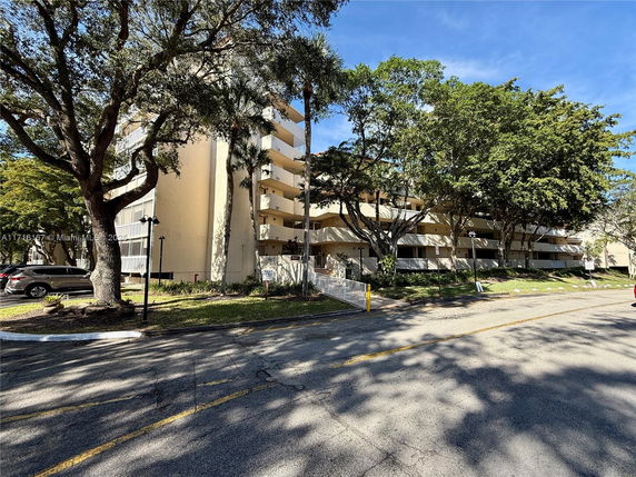Front view of a multi-story apartment building with balconies and surrounding trees.