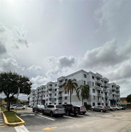 View of a multi-story residential building with an outdoor parking area in front.