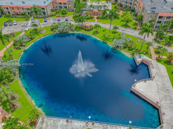 Aerial view of a pond with a fountain surrounded by residential buildings and landscaped greenery.