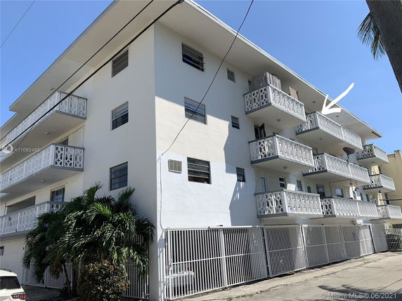Front view of a multi-story residential building with balconies and a gated area.