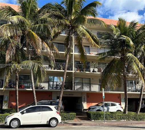 Front view of a multi-story building with balconies and palm trees.