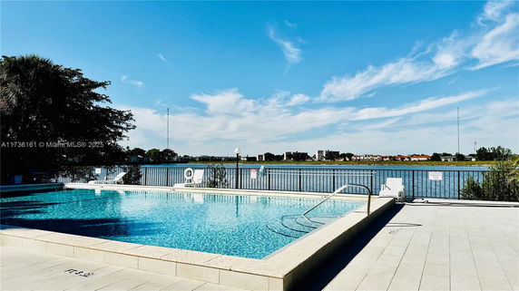 Outdoor swimming pool with a view of a lake and buildings in the background.