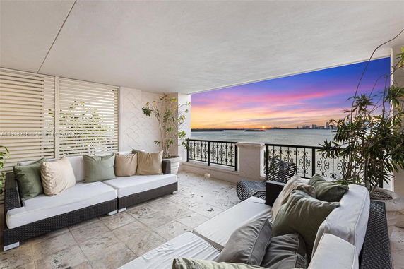 Outdoor patio with wicker sofas and cushions overlooking a scenic waterfront view at sunset.