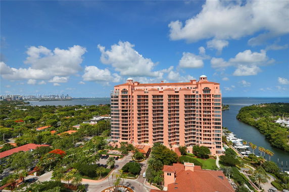 Tall pink building with balconies near water and greenery.