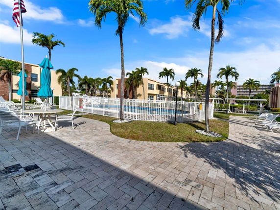 Outdoor swimming pool area surrounded by buildings and palm trees.