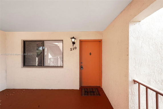 Entrance view of a building with an orange door marked 210 and a window beside it.