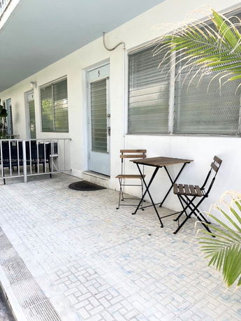 Front view of a building with a doorway and windows, featuring a small patio area with a table and chairs.