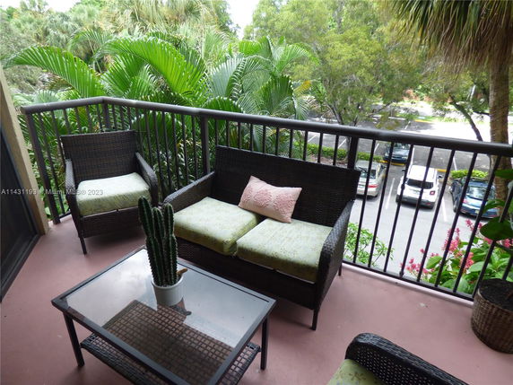View from a balcony overlooking a parking area and lush greenery.
