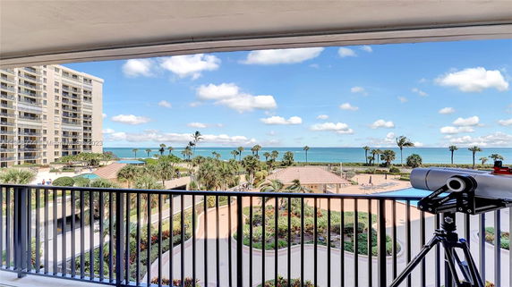 View from a balcony overlooking the ocean, a tall building, and landscaped area with a telescope in the foreground.