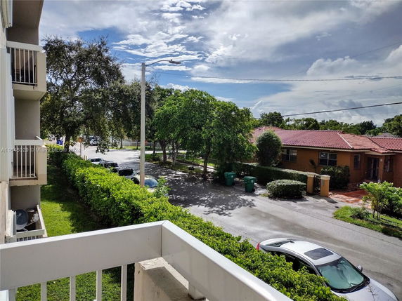 View from a balcony showing a street with houses, trees, and parked cars.