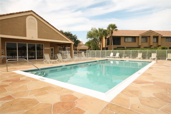 Outdoor swimming pool area with chairs and a building in the background.