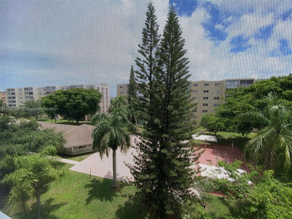 View through a window screen showing surrounding greenery and several multi-story residential buildings.