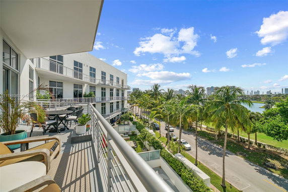 Panoramic view from a balcony showing a building facade and surrounding greenery with a cityscape in the background.
