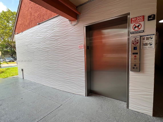 Exterior view of a building's elevator entrance with a textured wall and elevator signage.