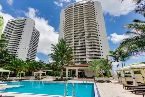 Front view of a tall, modern residential building with multiple balconies, viewed from a pool area.