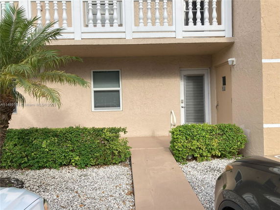 Front view of a beige stucco building with a door and window on the ground floor, and a balcony above.