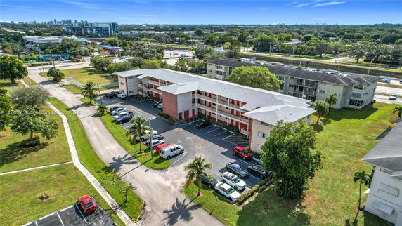 Aerial view of a multi-story residential building with parking area and surrounding greenery.