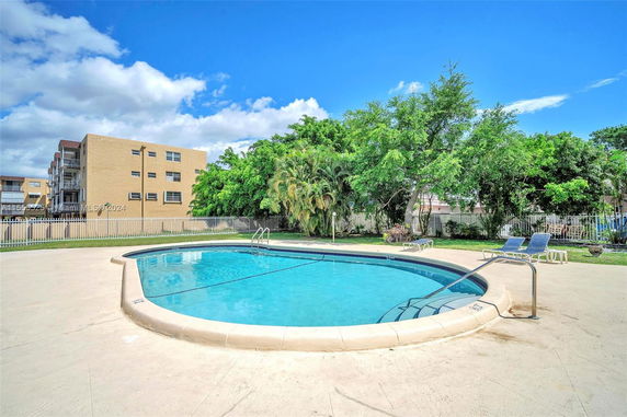 Outdoor swimming pool with adjacent building and trees.