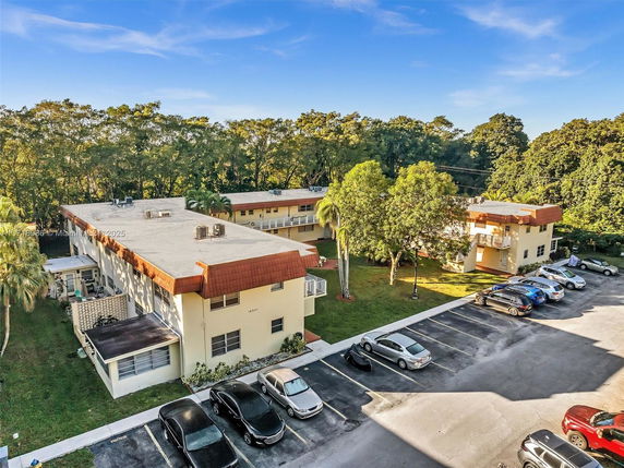 Aerial view of multiple residential buildings with parking area and surrounding trees.