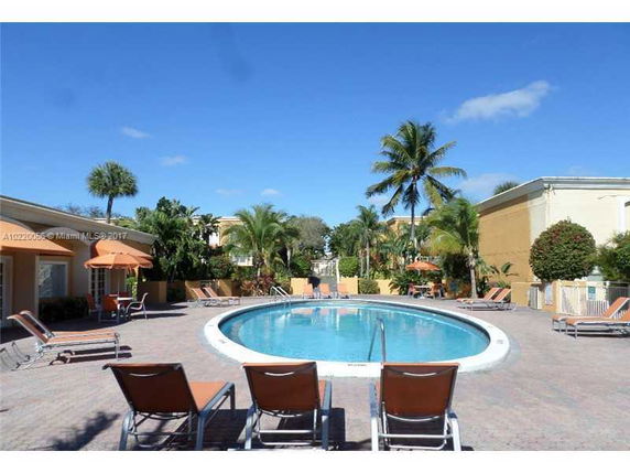 Outdoor swimming pool area with lounge chairs and umbrellas surrounded by palm trees.