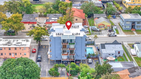 Aerial view of a multi-story building with parking and a swimming pool in a residential neighborhood.