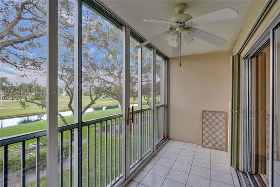 Balcony with ceiling fan overlooking green landscape and water body.