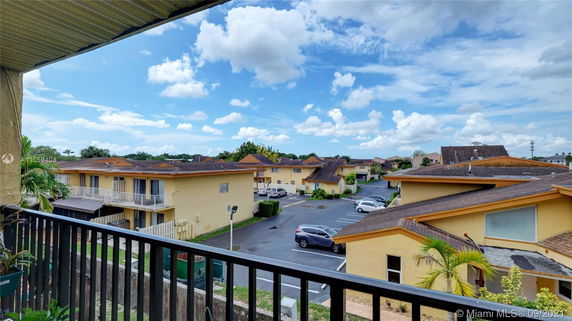 View from a balcony overlooking a residential area with multiple beige buildings and parking spaces.